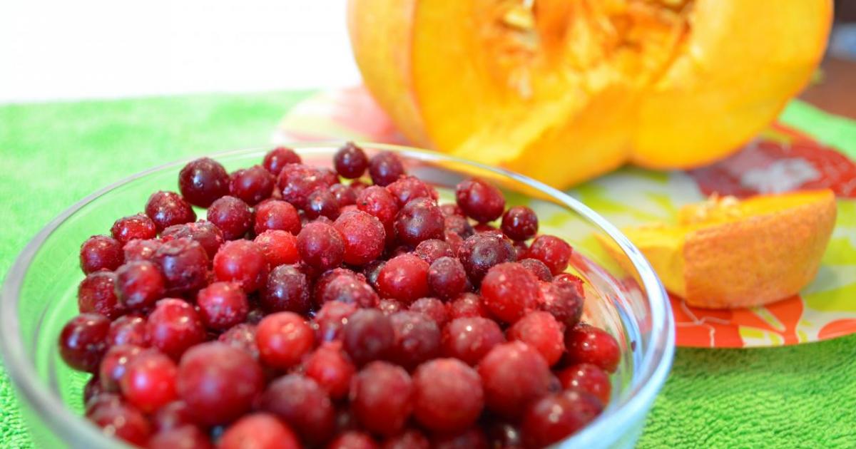 Свежезамороженная клюква в чашке с разрезанной тыквой
